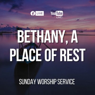 A boat rests on the sandy shore as the sun sets, casting warm hues across the sky and reflecting on the water.